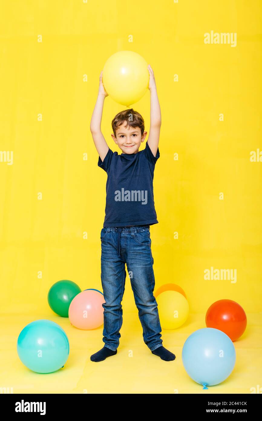 Portrait complet d'un garçon souriant tenant le ballon sur fond jaune Banque D'Images