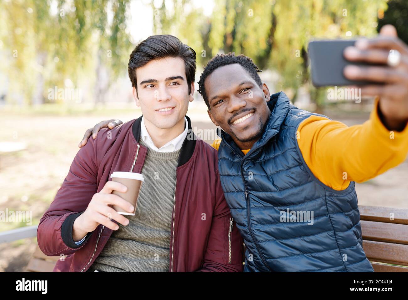 Deux jeunes hommes heureux assis sur le banc du parc prenant un selfie Banque D'Images