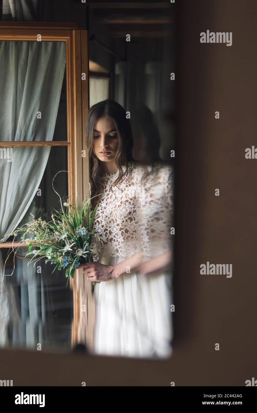 Jeune femme en robe de mariage élégante tenant un bouquet de vue vers le bas à la fenêtre Banque D'Images