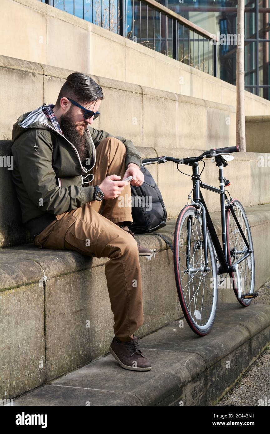 Side view of mid adult man using smart phone while sitting on steps in city Banque D'Images