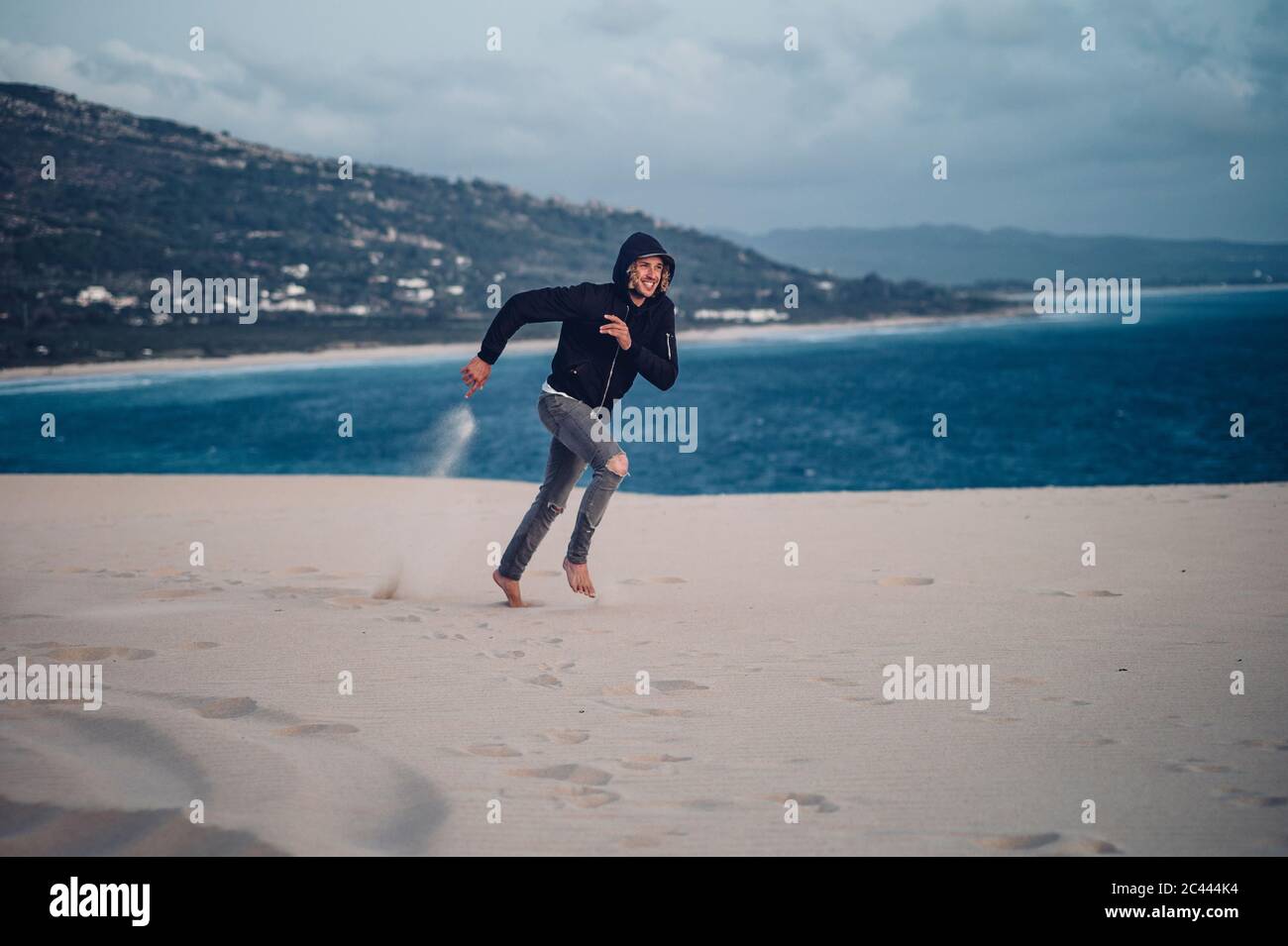 Pleine longueur d'homme courant à la plage contre le ciel à Tarifa, Espagne Banque D'Images