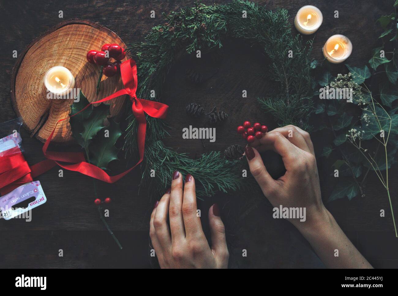 Femme mains faisant bricoler Yule solstice d'hiver (Noël) couronne de branches d'arbre à feuilles persistantes de cèdre. Placer les baies de houx dans elle. Pose à plat Banque D'Images