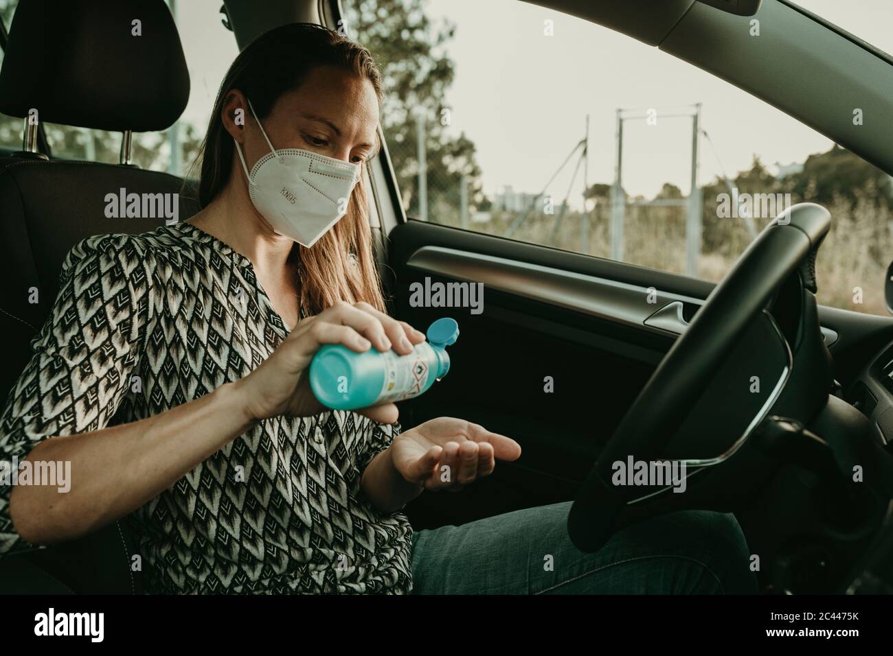 Femme adulte de taille moyenne avec masque de protection utilisant un assainisseur en voiture Banque D'Images