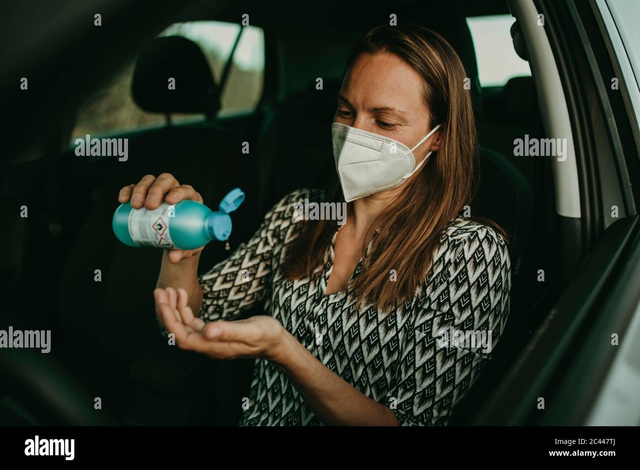 Femme adulte de taille moyenne avec masque de protection utilisant un assainisseur en voiture Banque D'Images