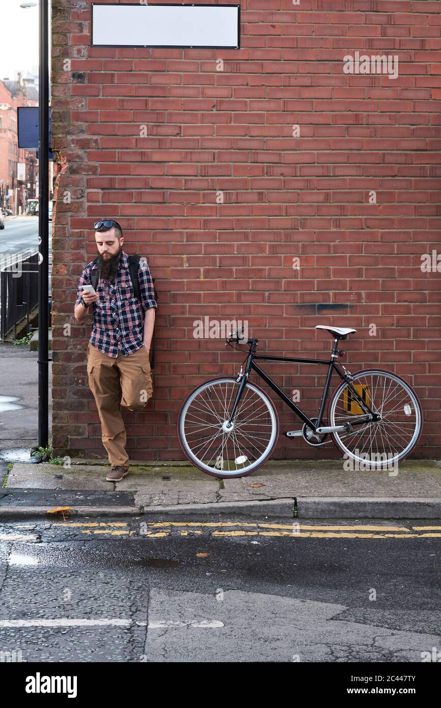 Bearded man using smart phone while standing against brick wall Banque D'Images