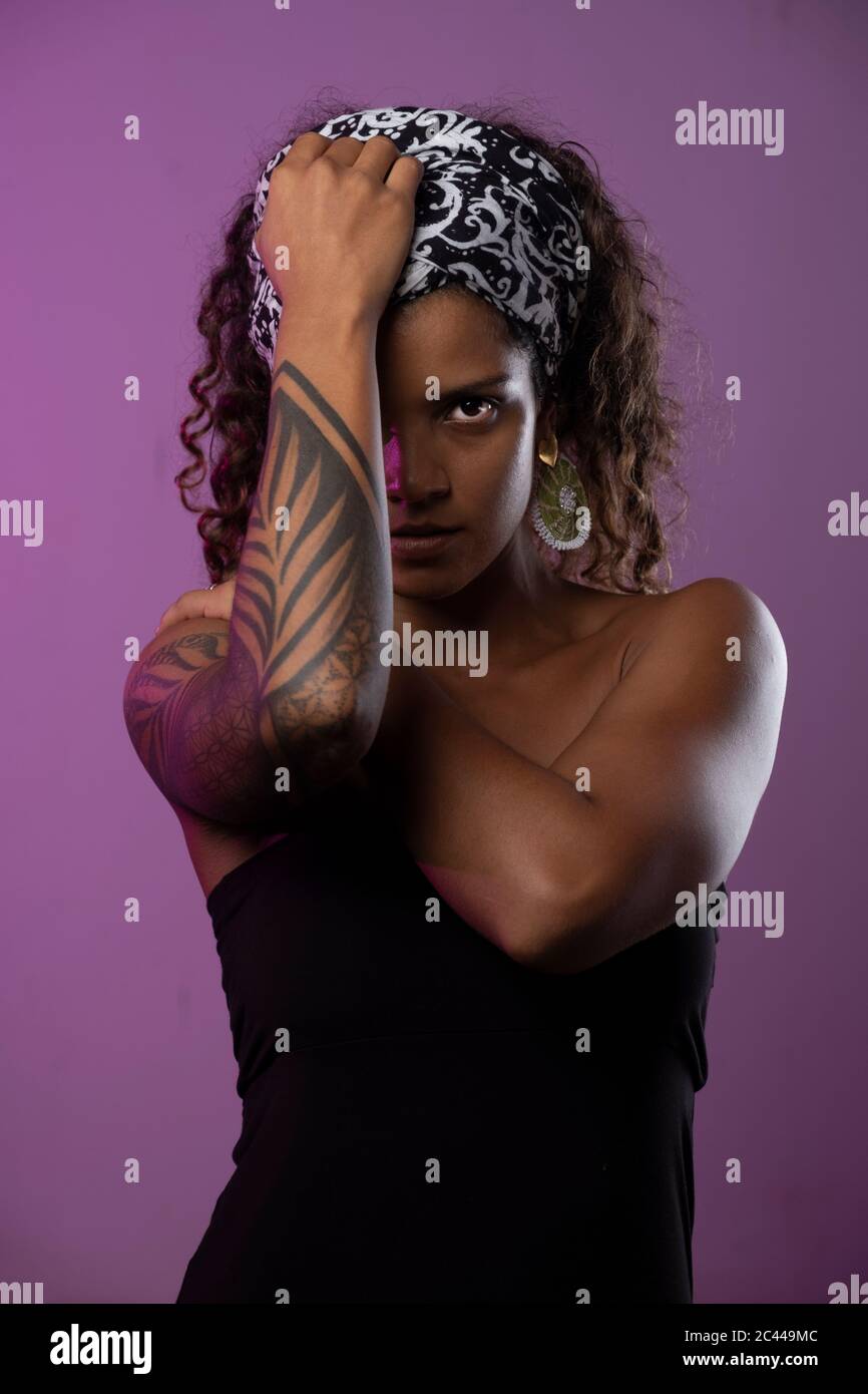 Portrait d'une jeune femme sérieuse avec bras tatoué sur fond violet Banque D'Images
