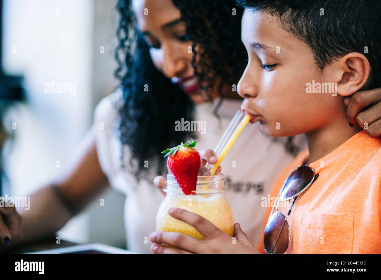 Gros plan sur le garçon qui boit du smoothie à la paille tout en étant assis près de sa mère au restaurant Banque D'Images