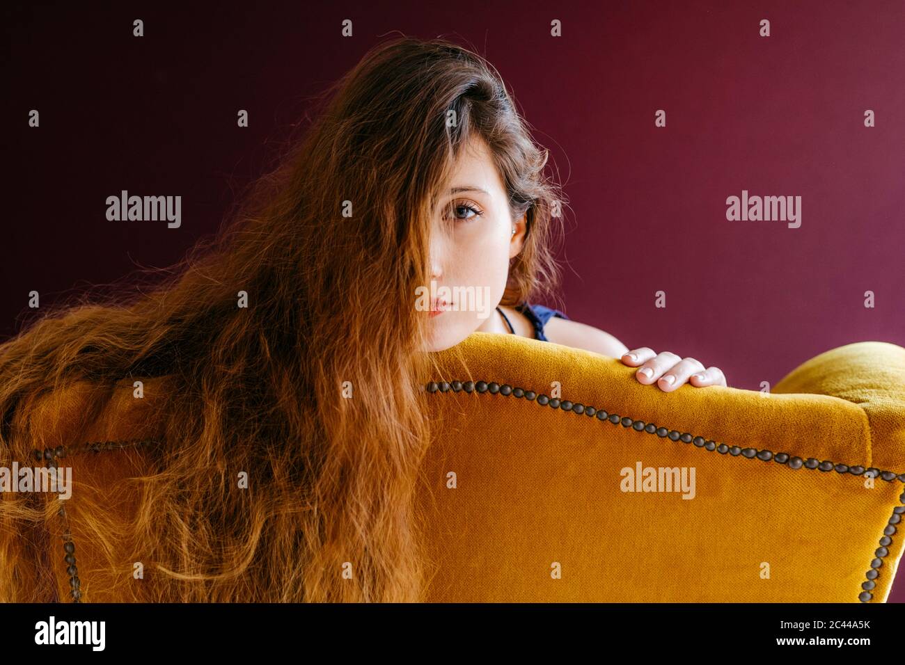 Portrait rapproché de la jeune femme avec de longs cheveux bruns, adochée sur une chaise dorée sur un fond coloré Banque D'Images