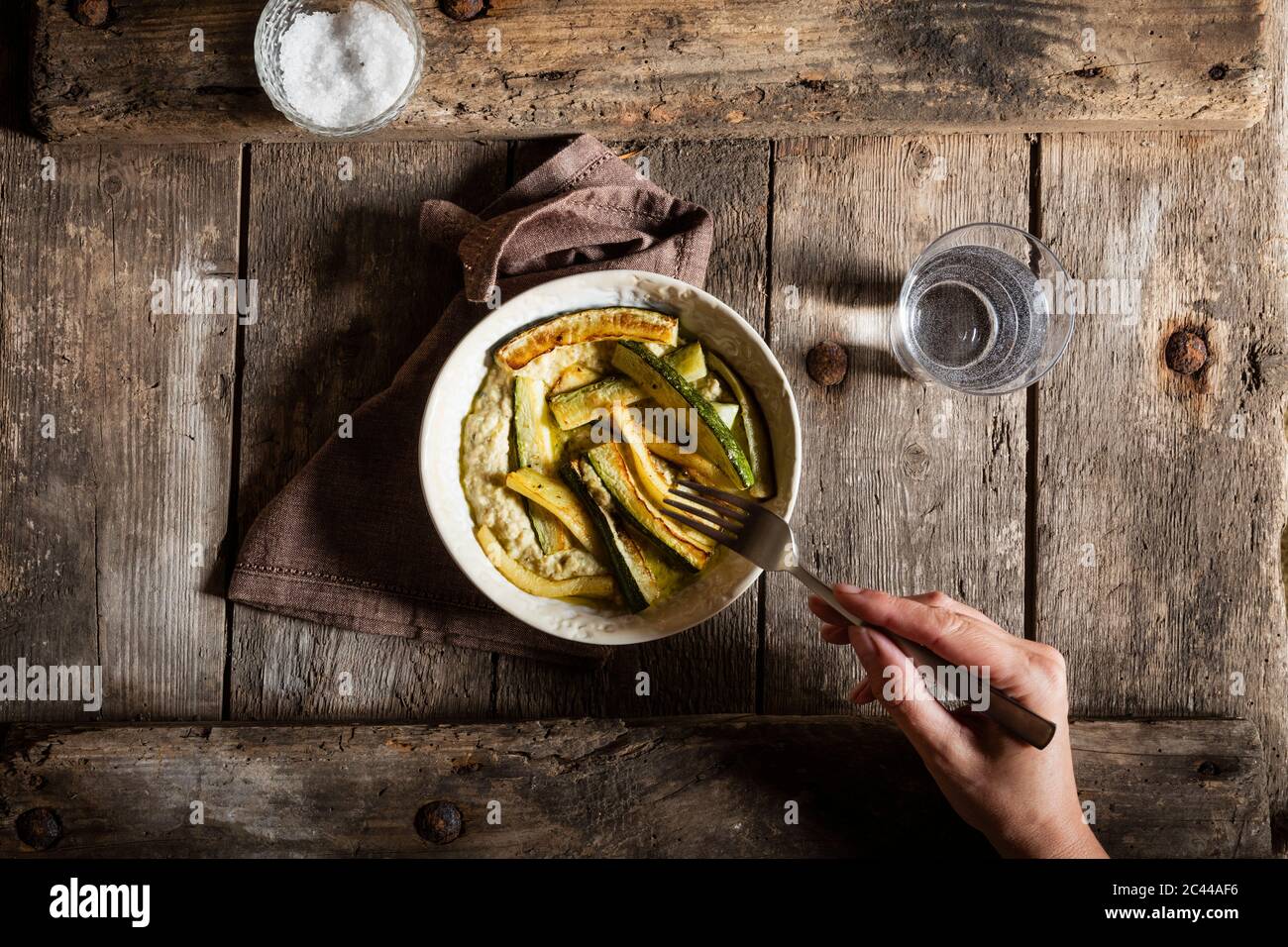 La main coupée de mature woman eating meal on wooden table Banque D'Images