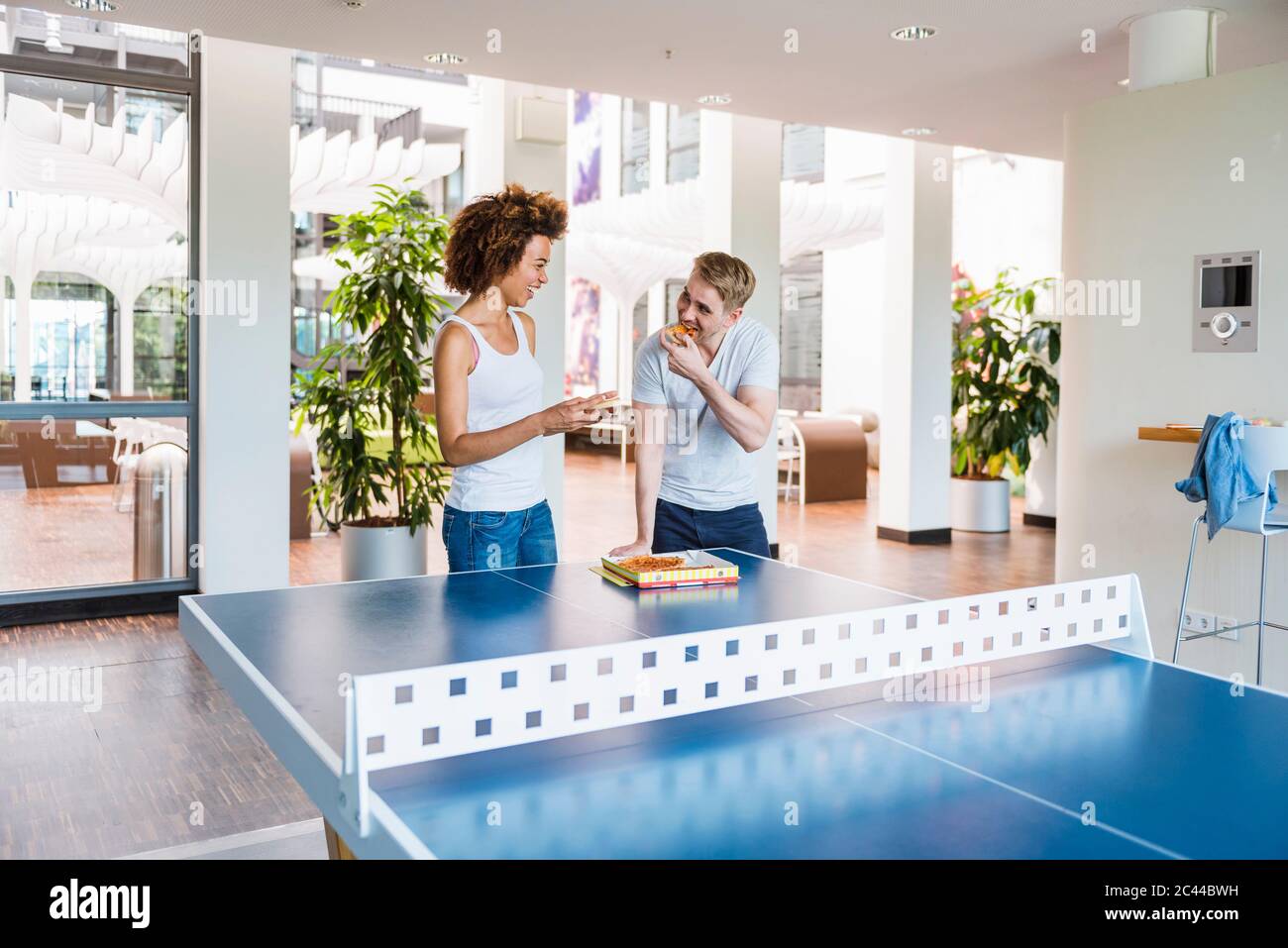Les jeunes gens d'affaires partagent une pizza pour le déjeuner dans un bureau moderne avec table de ping-pong Banque D'Images