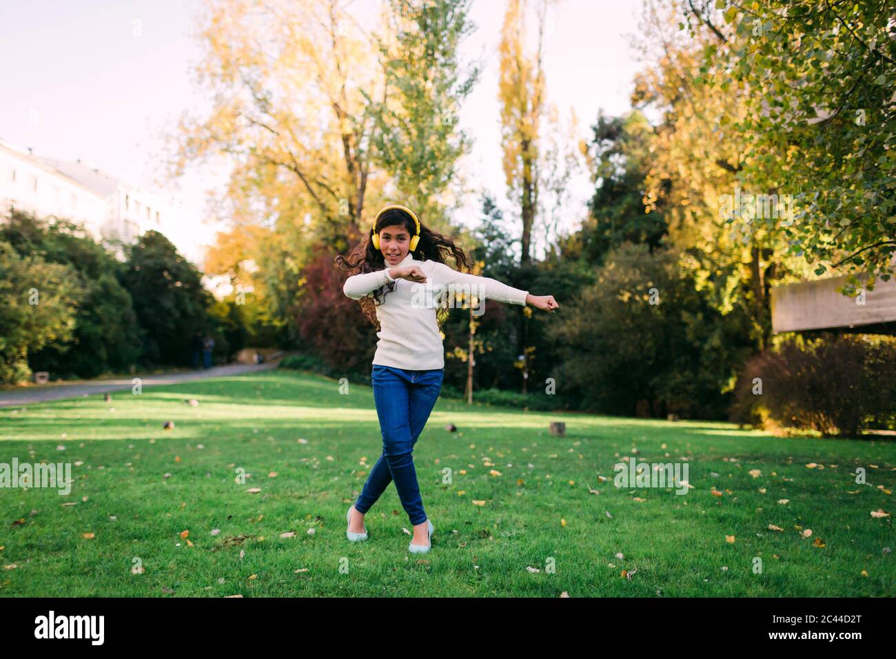 Bonne fille écoutant de la musique et dansant sur des terres herbeuses dans le parc pendant l'automne Banque D'Images