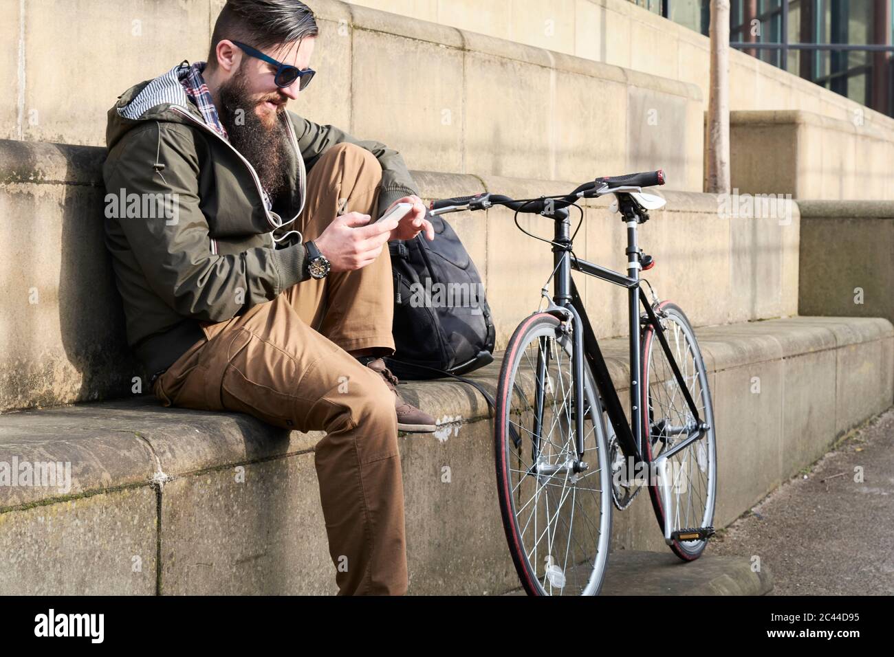 Vue latérale du bearded man using smart phone while sitting on steps in city Banque D'Images