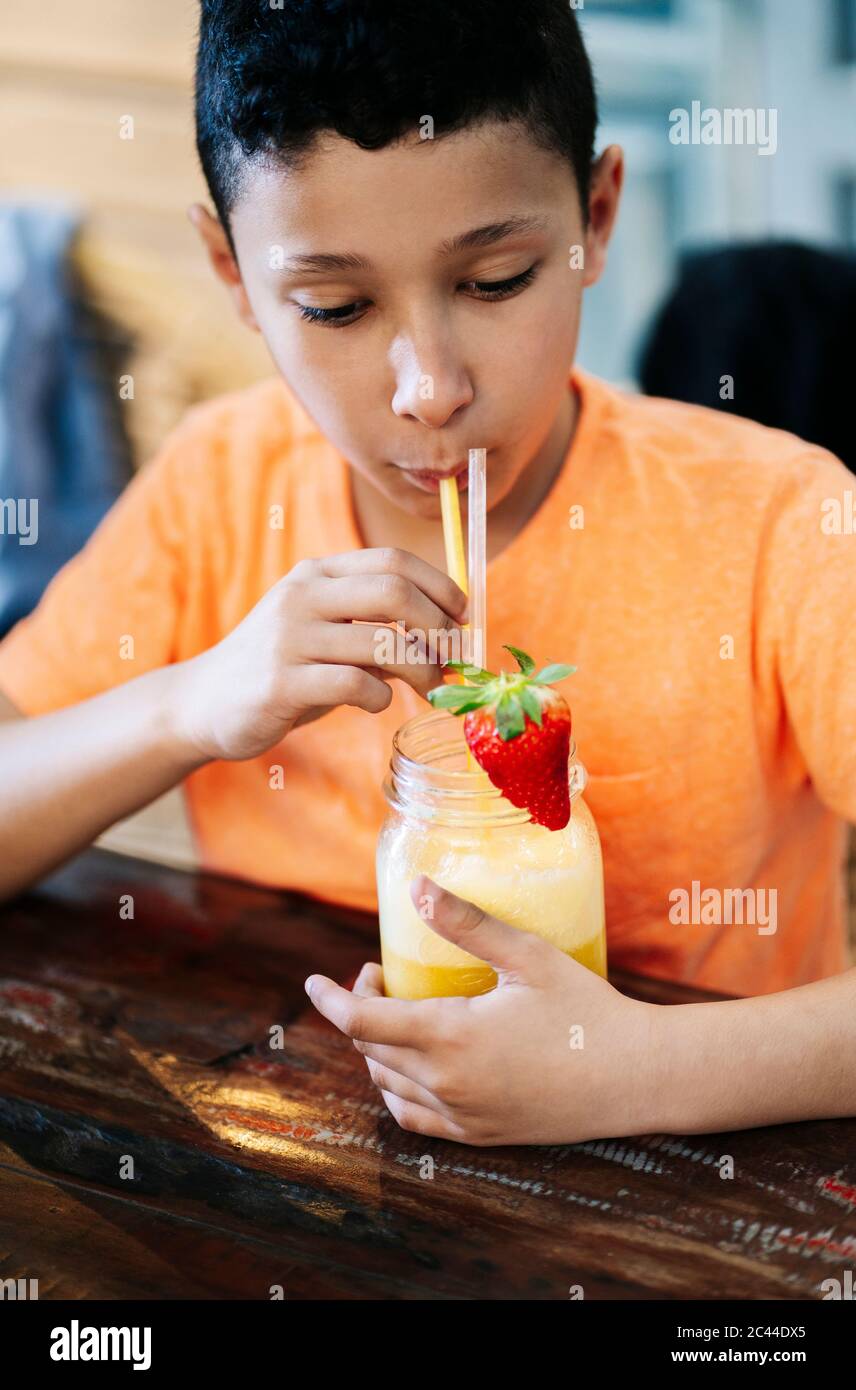 Garçon buvant du smoothie à la paille tout en étant assis à table dans le restaurant Banque D'Images