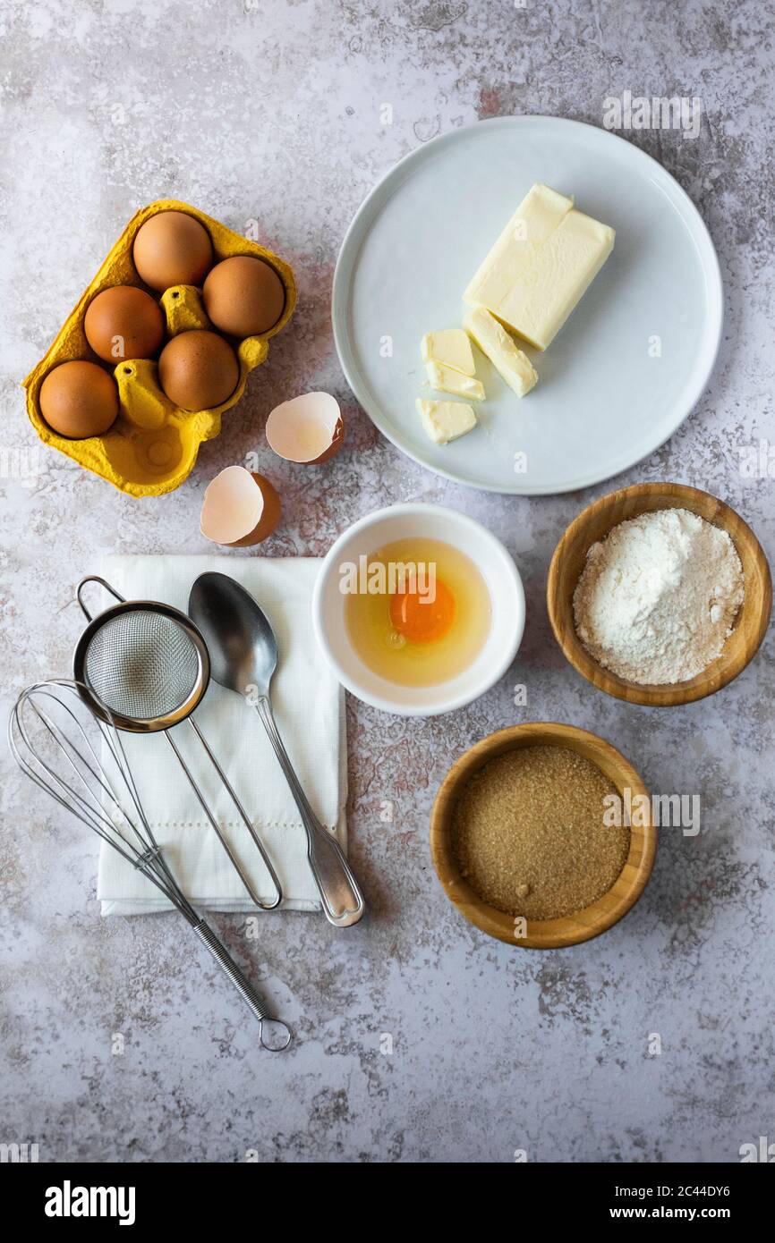 Oeufs de poulet, beurre, farine, cassonade, serviette, cuillère, tamis et fouet Banque D'Images