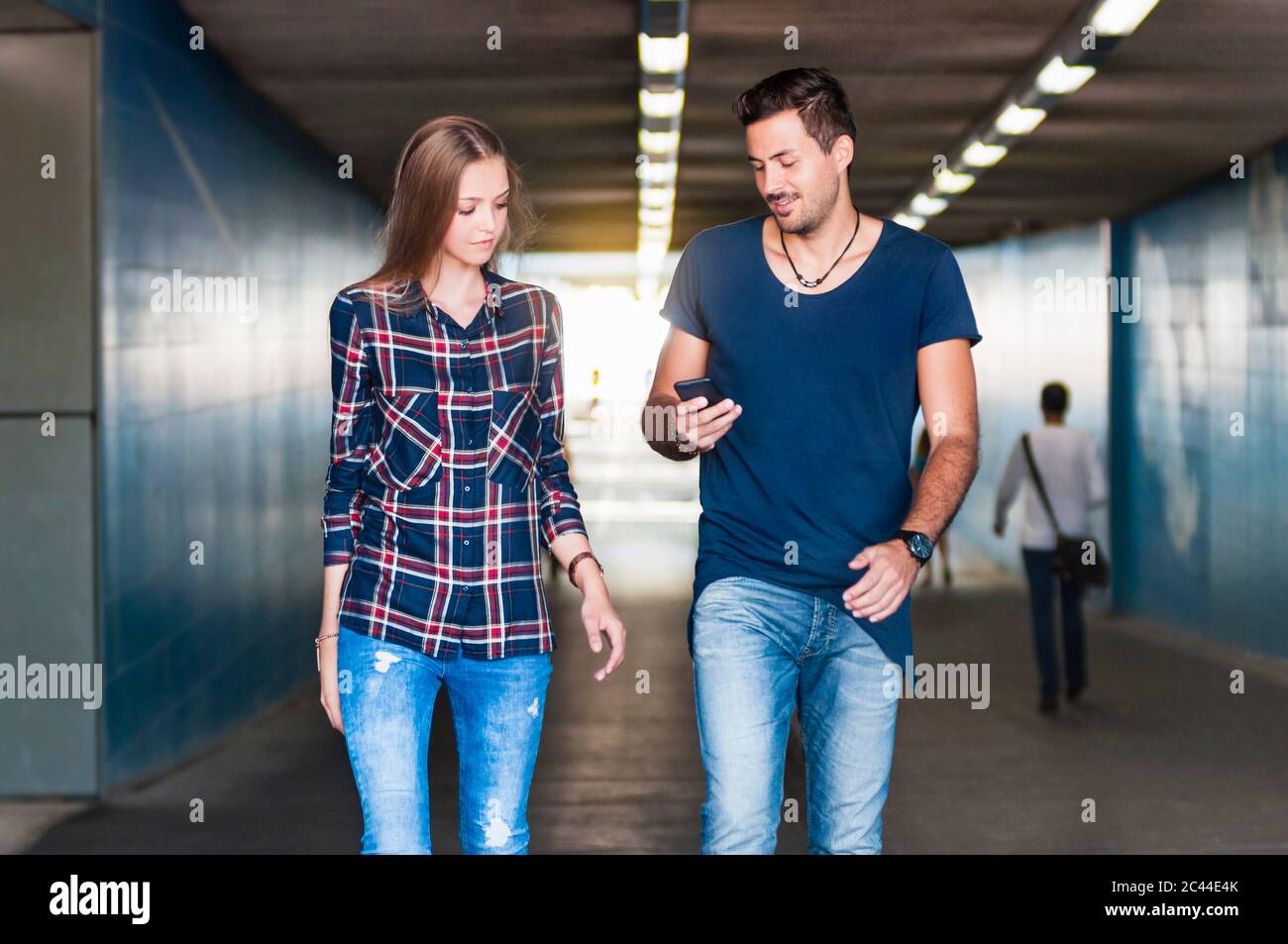 Un jeune homme et une jeune femme qui marchent ensemble dans un passage souterrain Banque D'Images Un jeune homme et une jeune femme qui marchent ensemble dans un passage souterrain Banque D'Images