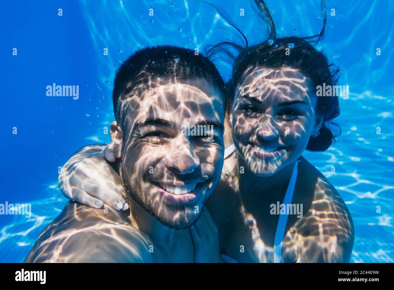 Jeune couple souriant nageant sous l'eau dans la piscine Banque D'Images