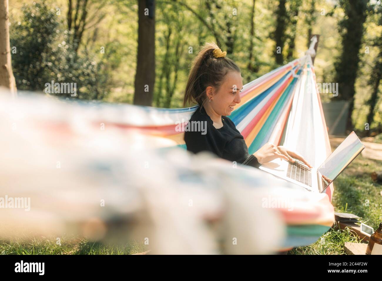 Jeune femme utilisant un ordinateur portable tout en étant assise sur un hamac dans la cour Banque D'Images