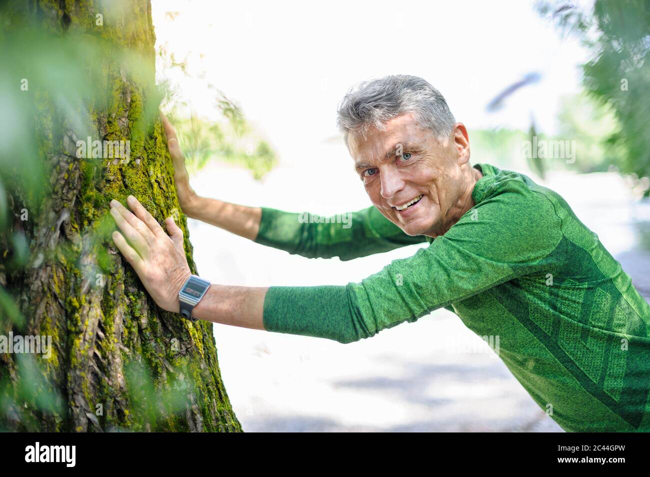 Portrait d'un homme âgé souriant qui s'exerce tout en s'appuyant sur le tronc d'arbre au parc Banque D'Images