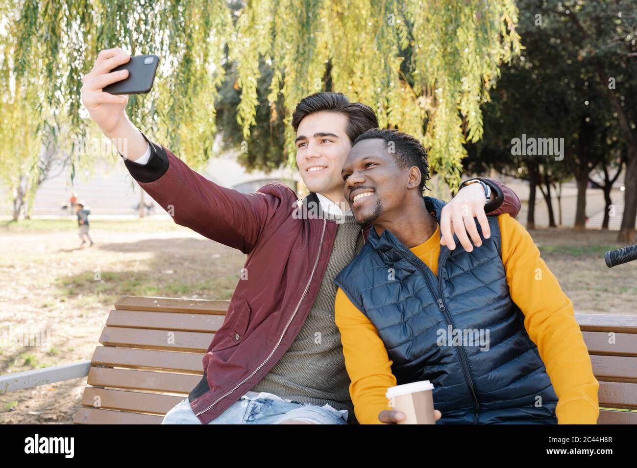 Deux jeunes hommes heureux assis sur le banc du parc prenant un selfie Banque D'Images