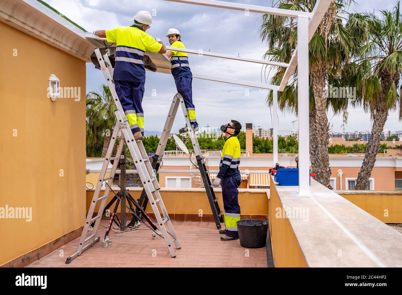 Homme regardant des collègues installer des panneaux solaires sur le toit en se tenant sur le balcon Banque D'Images
