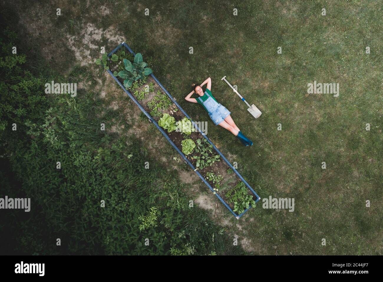 Tir de drone d'une femme avec les mains derrière la tête allongé par un lit surélevé sur la terre Banque D'Images