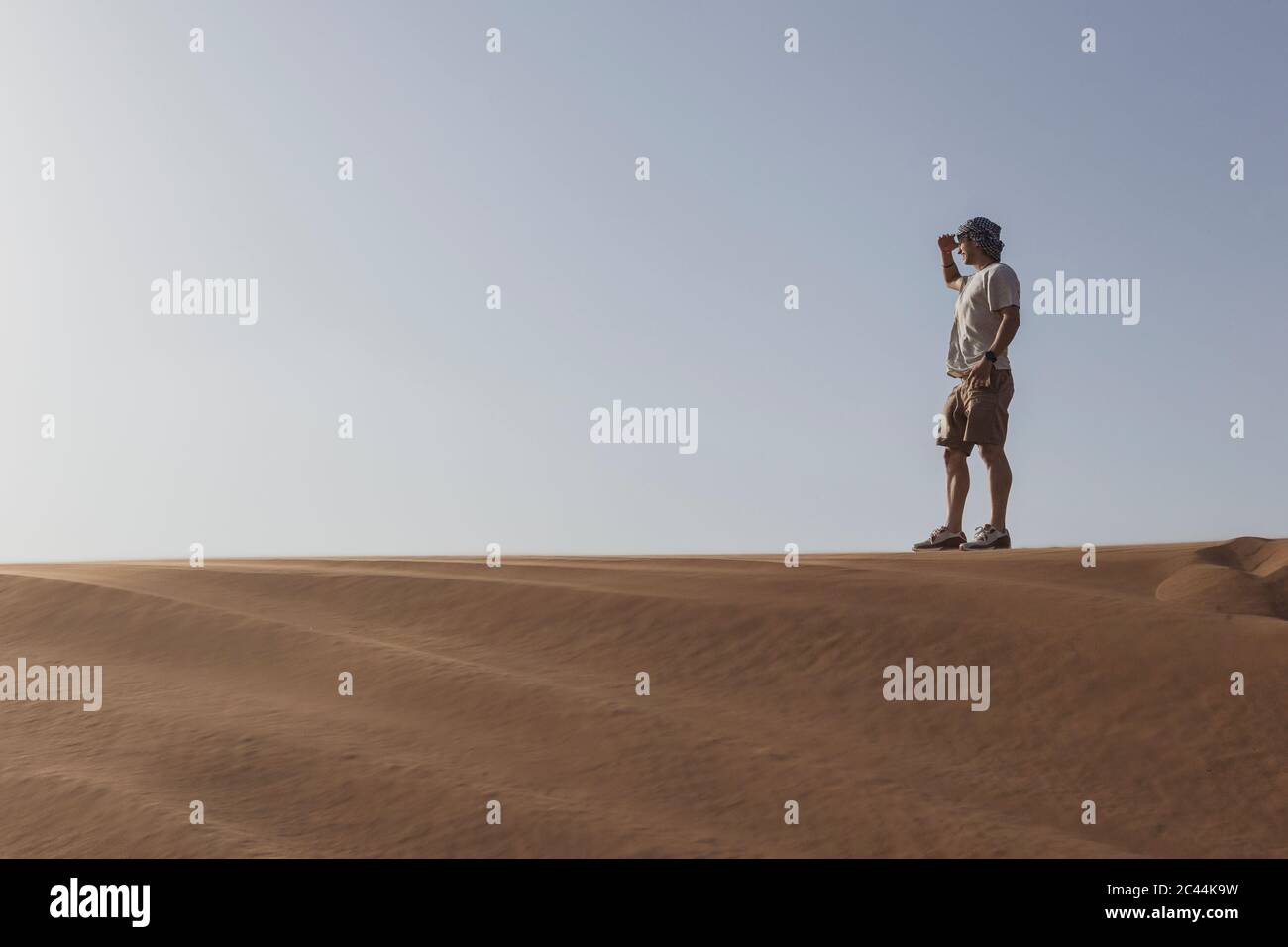 Les touristes mâles se protègent des yeux en se tenant sur une dune de sable contre un ciel dégagé à Dubaï, Émirats arabes Unis Banque D'Images