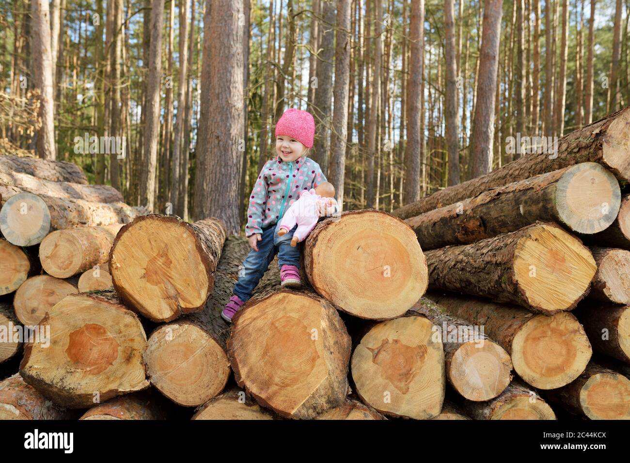 Petite fille souriante avec poupée assise sur une pile de bois dans la forêt Banque D'Images