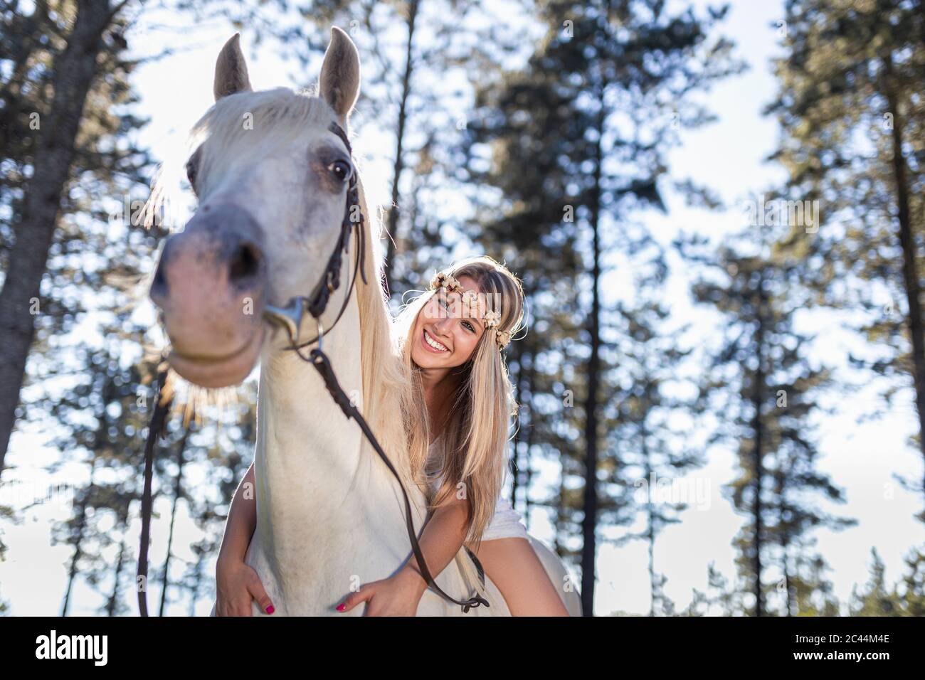 Vue en angle bas de la jeune femme souriante penchée sur un cheval blanc dans la forêt Banque D'Images