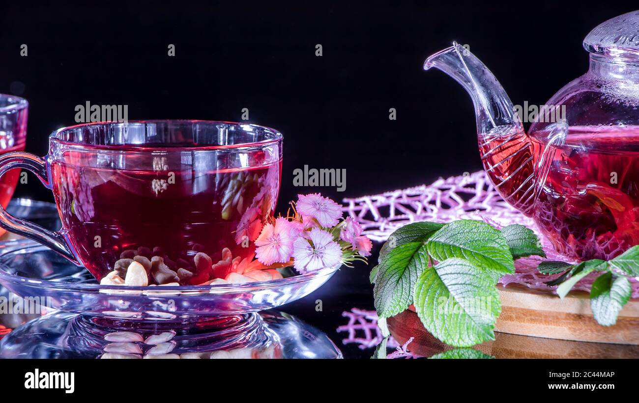 Une tasse de thé rouge et une théière en fleurs d'hibiscus blanc et feuilles vertes de thé médicinal sur un stand en bois.cérémonie du thé Zen. Photo de l'Indi rouge Banque D'Images