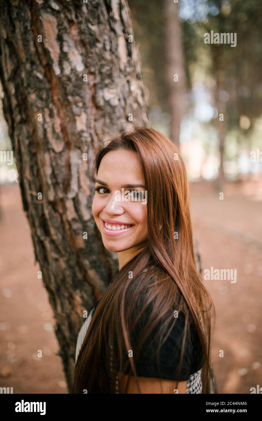 Portrait de la jeune femme souriante debout près du tronc d'arbre en forêt Banque D'Images