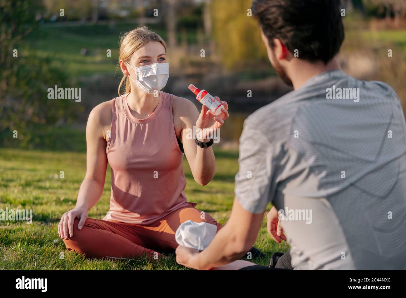 Femme portant un masque facial montrant de l'assainisseur pour les mains à l'homme pendant qu'elle est assise au parc Banque D'Images