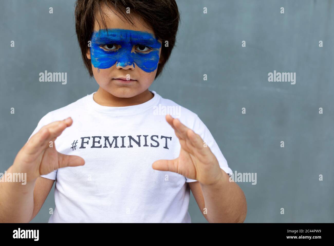 Portrait d'un garçon sérieux avec masque bleu peint sur son visage portant un t-shirt avec empreinte 'féministe' Banque D'Images