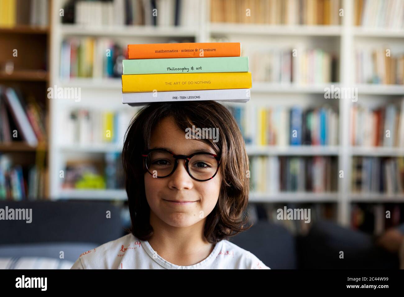 Portrait d'un garçon souriant équilibrant une pile de livres sur sa tête Banque D'Images