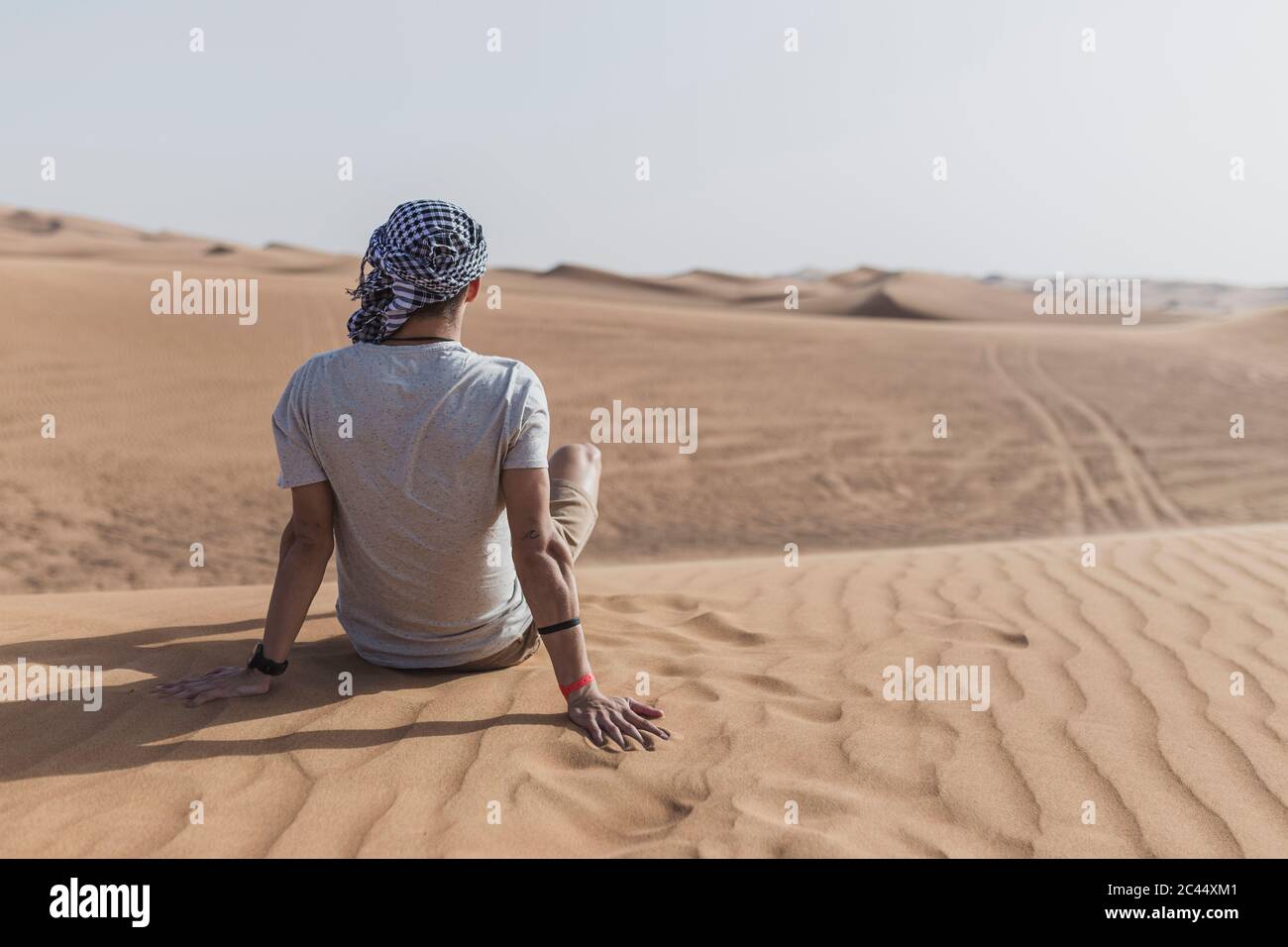 Jeune homme assis sur des dunes de sable dans le désert à Dubaï, Émirats arabes Unis Banque D'Images