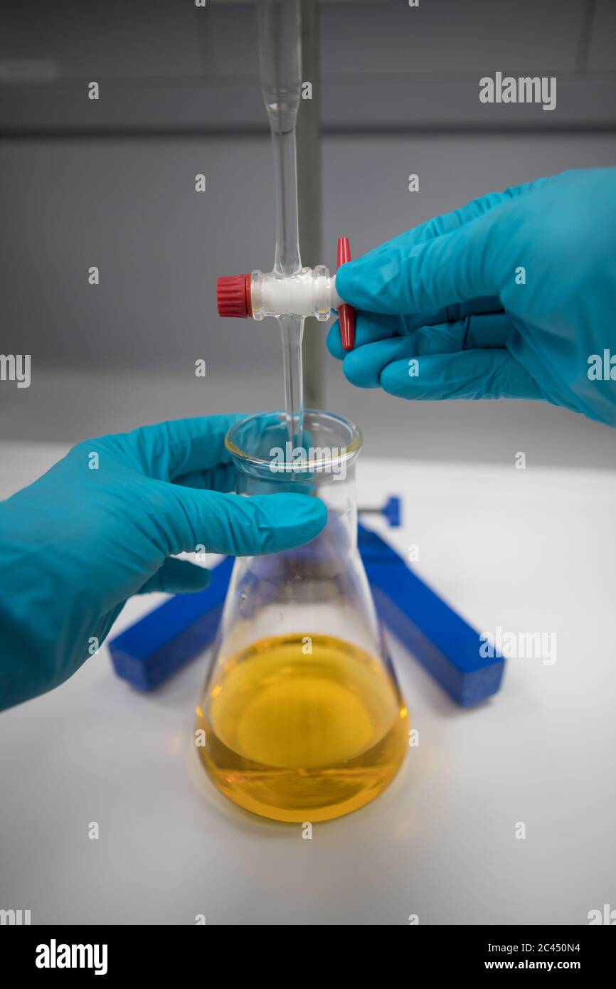 Chimiste avec mains gantées dans un laboratoire analysant un échantillon par titrage Banque D'Images