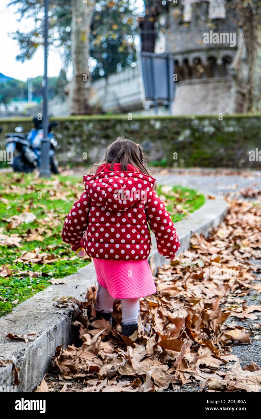 une petite fille, avec un manteau rouge à pois, joue avec les feuilles  séchées, tombées en hiver. A Grottaferrata, Rome, Italie, près de l'abbaye  de San Nilo, in Photo Stock - Alamy