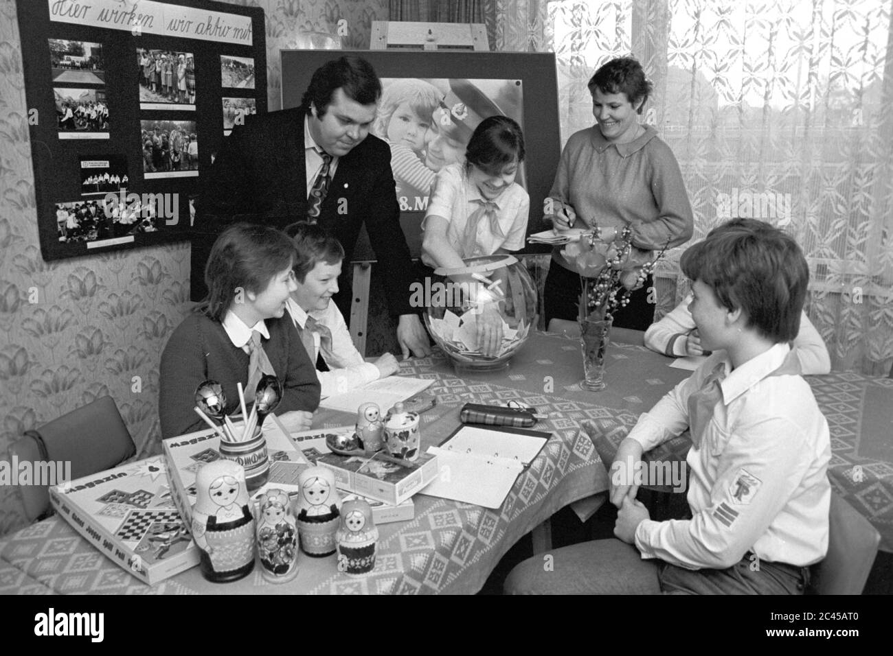 11 juillet 1985, Saxe, Delitzsch: Les prix d'une compétition sont raflés au milieu des années 1980 en présence d'un "officiel" de jeunes pionniers et de pionniers Thälmann portant des mouchoirs pionniers à la station de jeunes techniciens et touristes. Au premier plan, il y a des matryoshkas sur la table, au fond il y a une affiche du jour de la libération (8 mai) avec un soldat soviétique avec un enfant dans ses bras. Date exacte de la photo inconnue. Photo: Volkmar Heinz/dpa-Zentralbild/ZB Banque D'Images