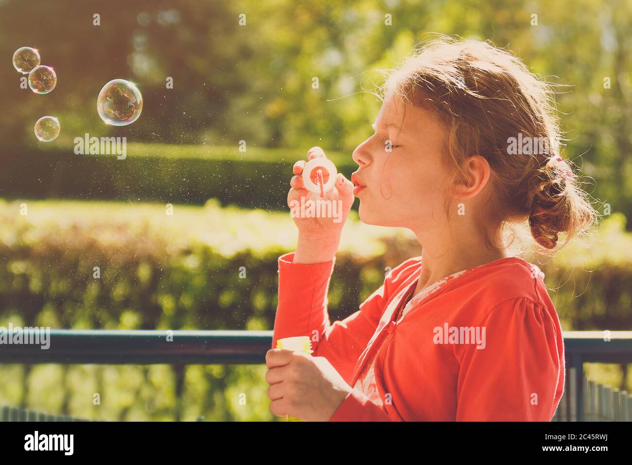 Jeune fille portant une veste orange soufflant des bulles dans le parc pendant la lumière de l'heure d'or Banque D'Images