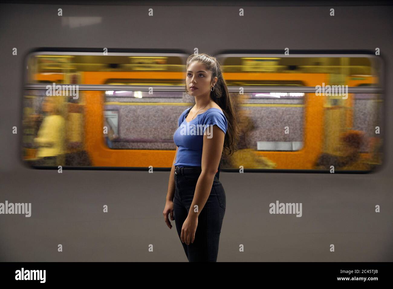 Jeune femme aux cheveux longs et bruns debout devant le train de banlieue sur la plate-forme de la gare. Banque D'Images