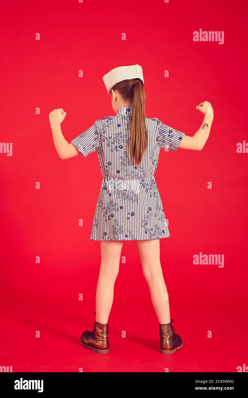 Vue arrière de la fille brune portant une robe bleue et un chapeau de marin sur fond rouge. Banque D'Images