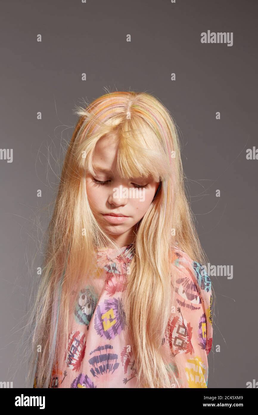 Portrait d'une fille aux cheveux longs blonds portant une robe de monstre à pompons roses, sur fond gris. Banque D'Images