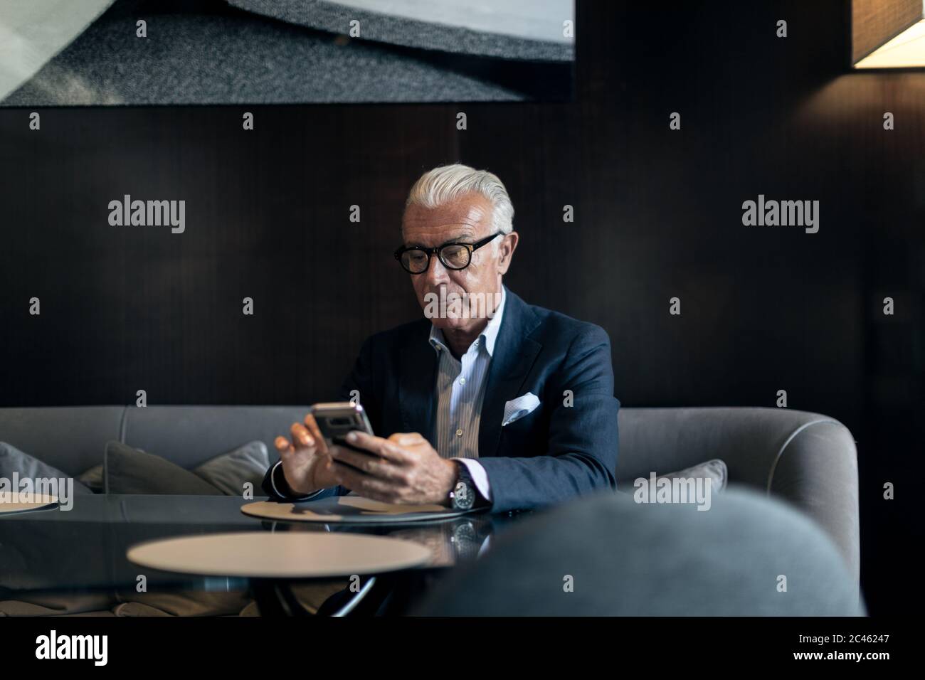 Senior businessman sitting in hotel table en utilisant l'écran tactile du smartphone Banque D'Images