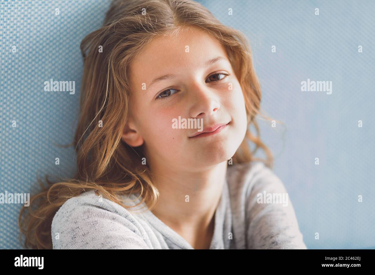 Portrait clair et aéré de la jeune fille souriant à l'appareil photo devant un fond bleu Banque D'Images