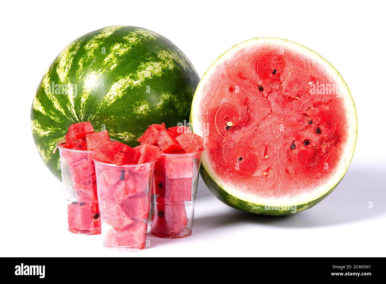 cubes de pastèque rouge en tranches dans une tasse en plastique avant de pastèque verte fraîche biologique et demi de pastèque coupée en tranches de texture rouge. Banque D'Images