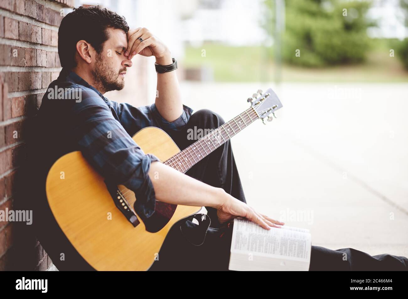 Triste homme assis sur le sol tenant un livre et une guitare Banque D'Images