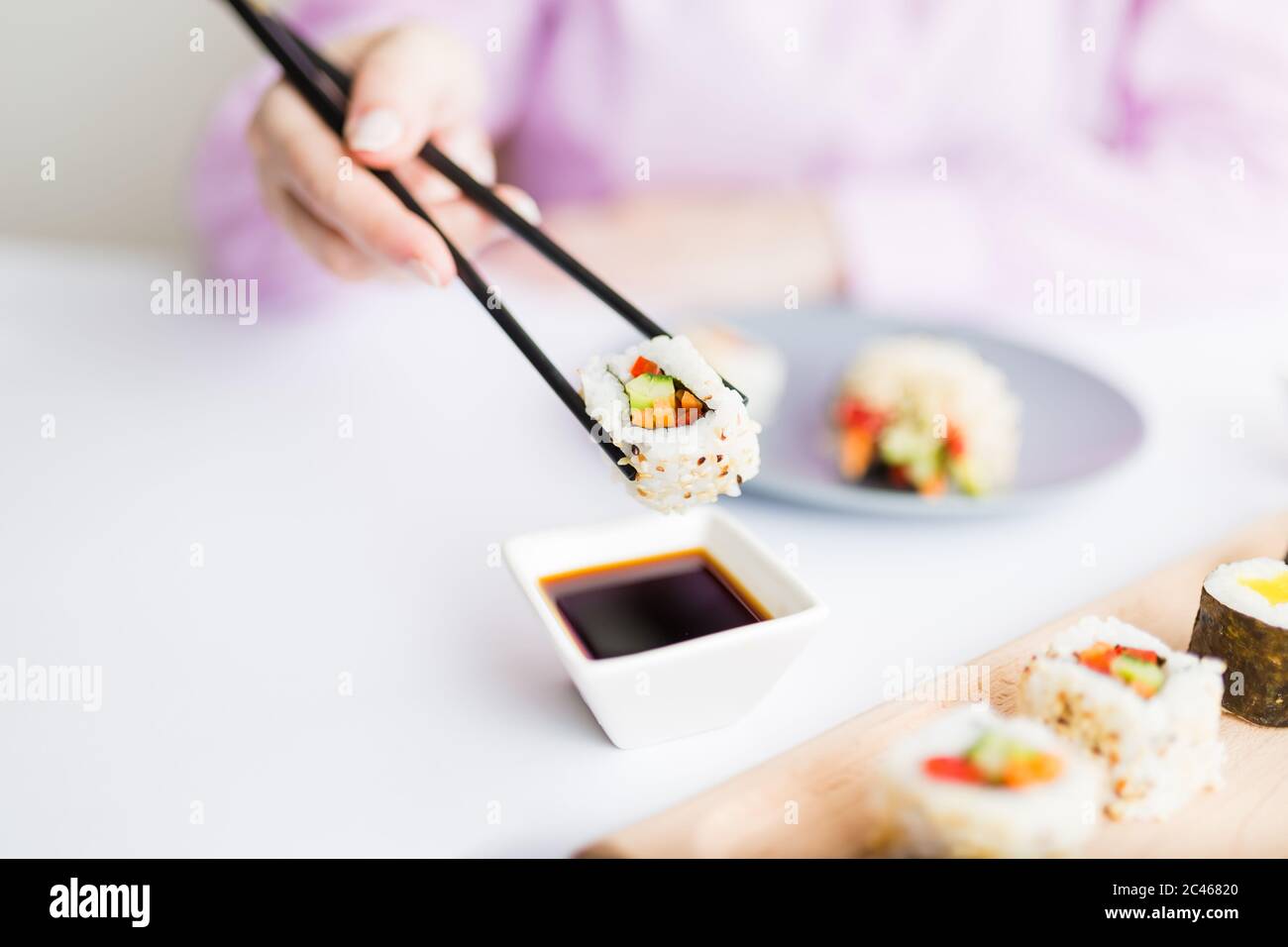Gros plan de la femme tenant un rouleau de sushi avec des baguettes au-dessus d'un bol rempli de sauce soja. Concept de repas japonais traditionnel sain. Banque D'Images