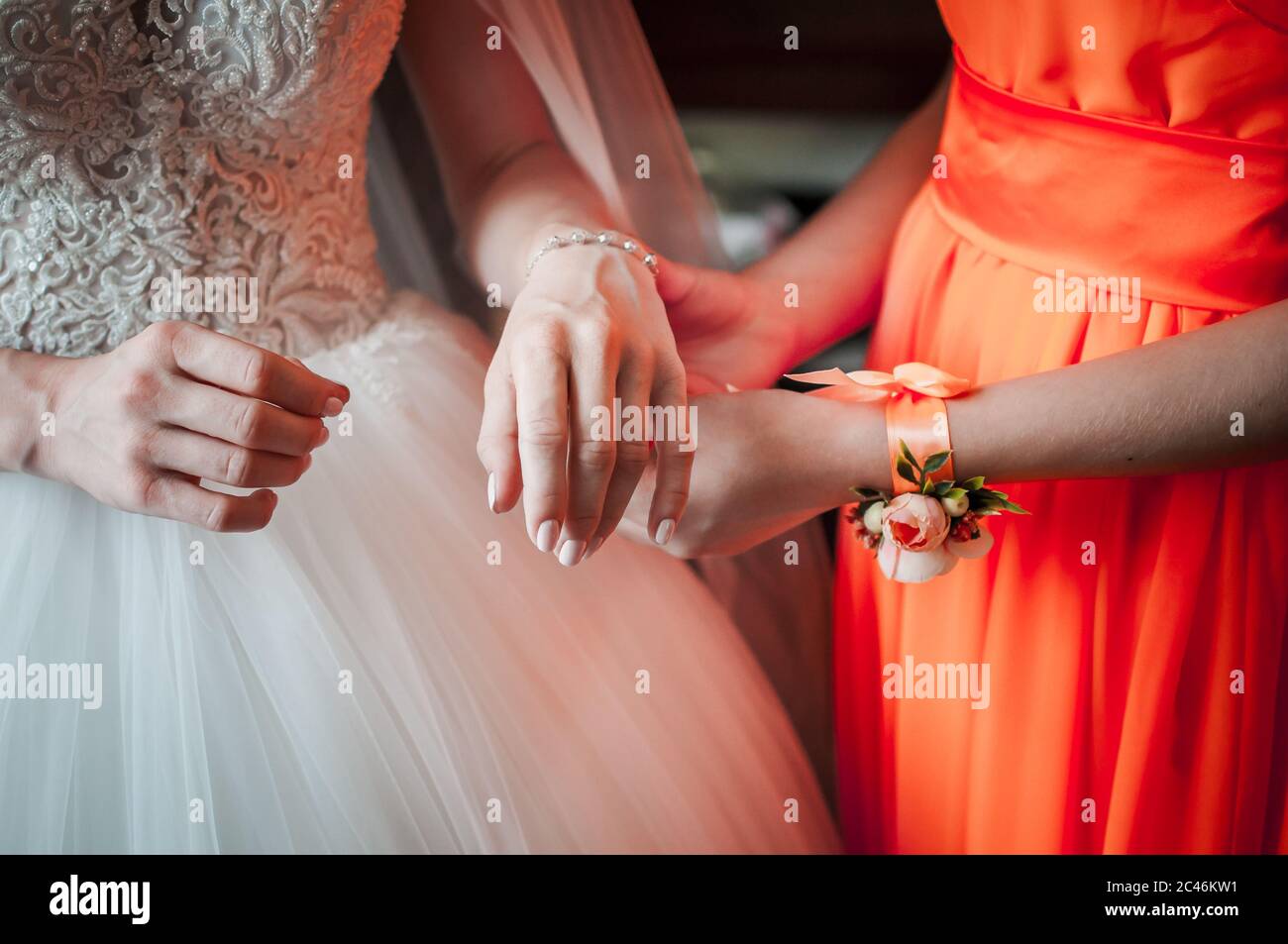 La demoiselle d'honneur en robe orange aide la mariée à porter un bracelet Banque D'Images