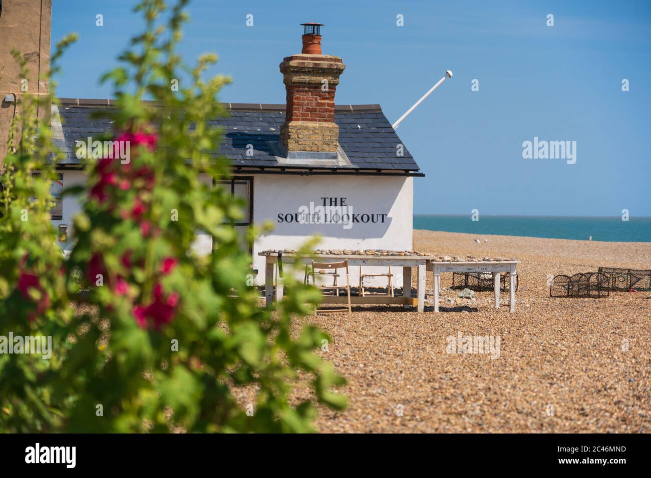 Vue sur le South Lookout avec des hollyhocks en premier plan situé sur la plage d'Aldeburgh, Suffolk. ROYAUME-UNI Banque D'Images