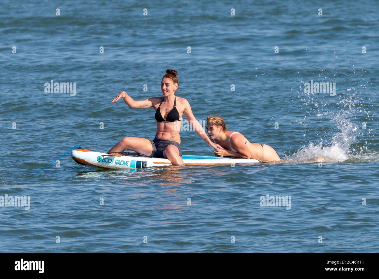 Chalkwell, Southend on Sea, Essex, Royaume-Uni. 24 juin 2020. Avec les températures records de l'année de prévision, les gens se dirigent vers le front de mer pour se rafraîchir, pendant la période d'alerte de séjour du coronavirus COVID-19. À Chalkwell, à l'ouest de Southend on Sea, la rive de l'estuaire de la Tamise est occupée par des paddle-boarders et des nageurs. Deux femelles blanches de race blanche sur un conseil, dont une frappe pour la propulsion Banque D'Images