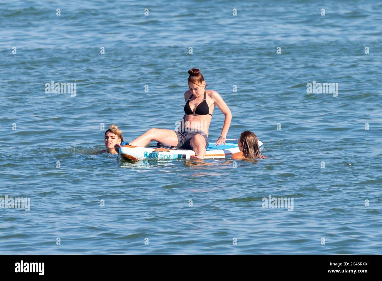 Chalkwell, Southend on Sea, Essex, Royaume-Uni. 24 juin 2020. Avec les températures records de l'année de prévision, les gens se dirigent vers le front de mer pour se rafraîchir, pendant la période d'alerte de séjour du coronavirus COVID-19. À Chalkwell, à l'ouest de Southend on Sea, la rive de l'estuaire de la Tamise est occupée par des paddle-boarders et des nageurs. Trois femelles blanches de race blanche avec une planche Banque D'Images